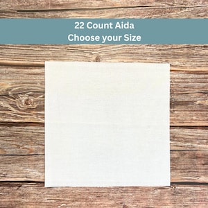 May include: A square piece of white 22 count Aida fabric for cross-stitch projects. The fabric features a visible grid-like weave pattern. Text overlay at the top reads 22 Count Aida Choose your Size against a muted blue background.