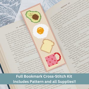 May include: A cross-stitch bookmark kit with a pattern and all supplies. The bookmark features a pink mug with hearts, a slice of toast, a fried egg, and an avocado. The text "Full Bookmark Cross-Stitch Kit Includes Pattern and all Supplies!!" is printed on the bottom of the bookmark.