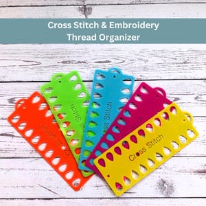 May include: A selection of brightly coloured cross stitch thread organisers in orange, green, blue, pink, and yellow. Each organiser has a series of holes and the words "Cross Stitch". The text "Cross Stitch & Embroidery Thread Organizer" is at the top.