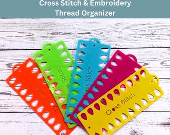May include: A collection of colorful cross stitch thread organizers in orange, green, blue, pink, and yellow. Each organizer has a series of holes and the words "Cross Stitch" printed on them. The text "Cross Stitch & Embroidery Thread Organizer" is at the top.