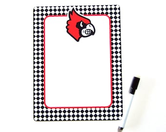 May include: A black and white checkered dry erase board with a red cardinal mascot in the top corner. The board has a red border and a white writing surface.