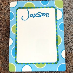 May include: A blue and green card with white polka dots and a green and blue border. The card has the name "Jaxson" written in cursive on it.