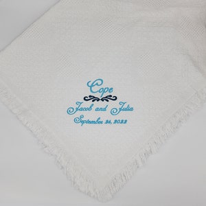 Pode incluir: Uma manta branca texturizada com bordas de franjas apresentando texto bordado em azul que diz Cope, Jacob and Julia, e September 24, 2022, com um detalhe decorativo azul-escuro centralizado entre a primeira e a segunda linha.