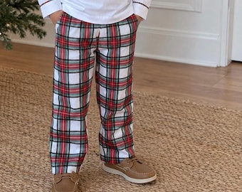 May include: A white long-sleeved shirt with plaid cuffs and matching plaid trousers featuring a red, green, and white tartan pattern. The trousers have side pockets and a straight-leg cut. The outfit is paired with tan leather slip-on shoes.