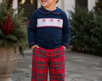 Puede incluir: Una camisa de manga larga azul marino con un panel frontal blanco fruncido que presenta caras de Papá Noel bordadas, un cuello redondo con ribete rojo, y pantalones de cuadros rojos, verdes y azules con zapatos de cuero blanco.
