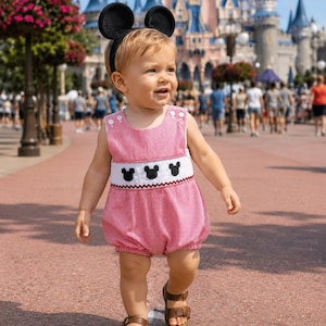 May include: A red and white gingham bubble romper featuring a white smocked chest panel with three black Mickey Mouse head silhouettes, paired with black mouse ear headband and brown leather sandals with two adjustable buckle straps.