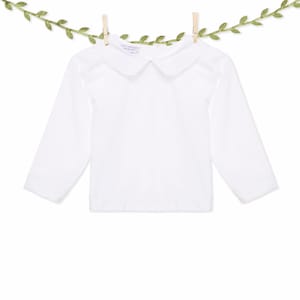 Puede incluir: Camisa blanca de manga larga con cuello Peter Pan. La camisa tiene una pequeña etiqueta que dice "Lil' Peanut" en el cuello.