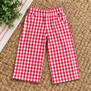 May include: A pair of pants featuring a red and white gingham check pattern. The pants have a straight-leg silhouette, a high-rise elasticized waistband, and two side pockets. The fabric displays a consistent checkered design throughout.