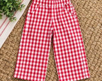 May include: A pair of pants featuring a red and white gingham check pattern. The pants have a straight-leg silhouette, a high-rise elasticized waistband, and two side pockets. The fabric displays a consistent checkered design throughout.