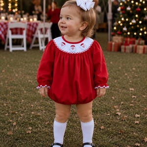 May include: A red long-sleeved bubble romper featuring a white round yoke with embroidered Santa Claus faces, a white ruffled collar, and white ruffled sleeve cuffs. The garment is paired with white knee-high socks and black patent leather shoes.