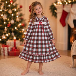 May include: A long-sleeved nightgown featuring a red, green, and white plaid pattern. The garment includes a ruffled collar, a white lace trim across the chest, a red ribbon bow at the center, and a ruffled hemline at the bottom edge.