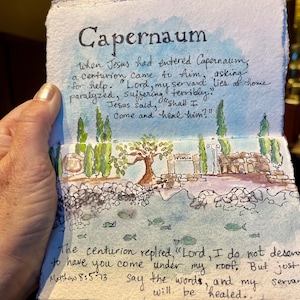 May include: Watercolor painting of Capernaum with text from Matthew 8:5-13. The artwork depicts a landscape with trees, water, and architectural elements. The title "Capernaum" is at the top, with handwritten text describing the biblical scene.
