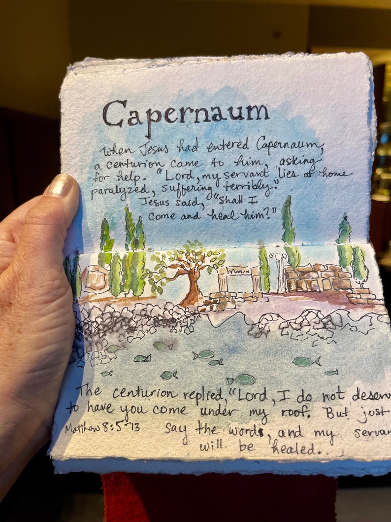 May include: Watercolor painting of Capernaum with text from Matthew 8:5-13. The artwork depicts a landscape with trees, water, and architectural elements. The title "Capernaum" is at the top, with handwritten text describing the biblical scene.