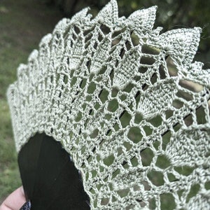 May include: A beige crocheted fan with a black handle. The fan is made of delicate lace and has a scalloped edge.