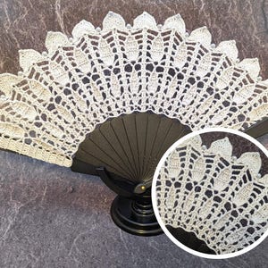 May include: A white crocheted fan with a black handle. The fan is decorated with small white beads.