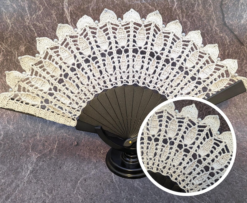 May include: A white crocheted fan with a black handle. The fan is decorated with small white beads.
