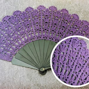 May include: A handcrafted, open purple crochet fan. The fan features a detailed, openwork design with a scalloped edge. The fan's base is a dark gray color. A circular inset shows a close-up of the crochet pattern.