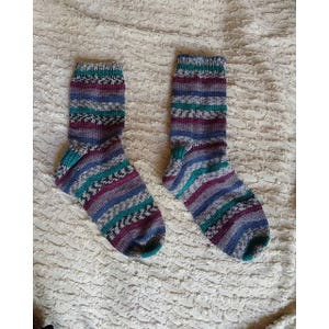 Pode incluir: Um par de meias listradas em tons de roxo, azul-turquesa e cinza. As meias são de malha e têm um aspeto texturizado.