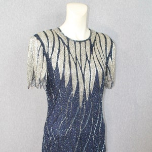Peut inclure: Une robe courte sans manches, en sequins, avec un motif argenté et bleu. La robe a un col rond et une silhouette ajustée.
