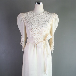 May include: A white maxi dress with a lace collar and trim. The dress has a sash tie at the waist and is made of a lightweight fabric.