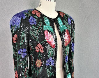 May include: Black sequin jacket with floral embroidery in red, blue, and green. The jacket has a turquoise sequin hem and shoulder accents, displayed on a mannequin.