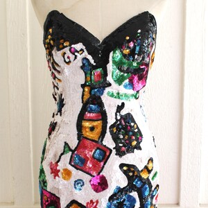 Peut inclure: Une robe de soirée sans bretelles en sequins avec une base blanche et des motifs abstraits colorés. La robe est faite de sequins de différentes couleurs, notamment rose, bleu, vert, jaune et rouge.