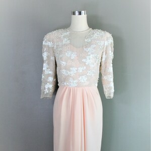 Peut inclure: Une robe de soirée formelle rose et blanche à paillettes avec un décolleté transparent et des manches trois-quarts. La robe a un corsage ajusté et une jupe fluide.
