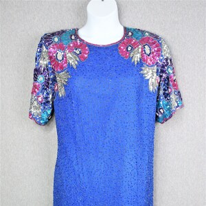 Peut inclure: Une robe bleu roi à paillettes avec des manches courtes et un col rond. La robe est décorée de broderies florales colorées.