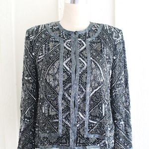 Könnte beinhalten: Eine schwarze und silberne Paillettenjacke mit geometrischem Muster. Die Jacke hat einen Reißverschluss und lange Ärmel.