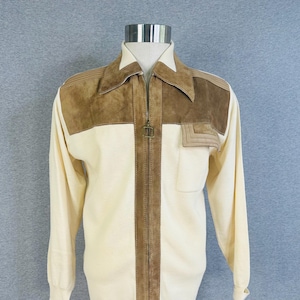 May include: A cream-colored long-sleeve jacket featuring brown suede panels on the chest and shoulders, a full-length front zipper with a metal pull, a pointed collar, and a single chest pocket with a decorative flap detail on the left side.