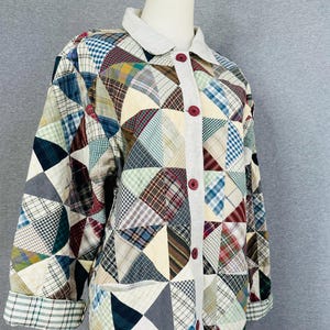 May include: A long-sleeved jacket featuring a patchwork design of various plaid and checkered fabric triangles in shades of blue, red, green, yellow, and white. The jacket has a solid light-colored collar, a front button placket with dark red buttons.