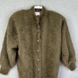 May include: An olive green fuzzy cardigan with a high collar and long sleeves. The garment features a front button closure with five circular buttons and ribbed cuffs. The texture is soft and brushed, providing a distinct appearance. A white label is visible at the inner neckline.