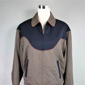 May include: A brown and navy blue jacket with a zipper closure. The jacket has a yoke design with a contrasting color and a decorative trim around the neckline.