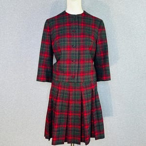 May include: A two-piece set consisting of a long-sleeved jacket and a pleated skirt, both featuring a red and dark green plaid pattern. The jacket has a round neckline and a front button closure, while the skirt features vertical pleats.