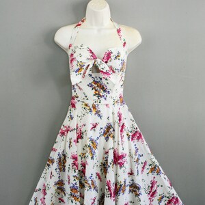 May include: A white halter dress with a floral print. The dress has a bow at the neckline and a fitted bodice. The skirt is full and flowing.
