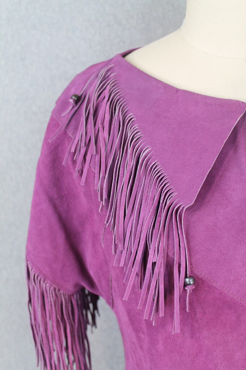 May include: A purple suede jacket with fringe detailing on the collar and sleeves.