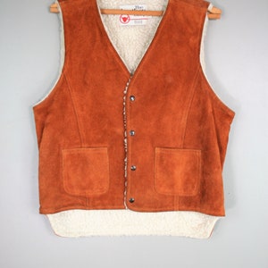 May include: A brown suede vest with a white sherpa lining. The vest has a button closure and two pockets. The label on the vest reads "The Leather Shop".