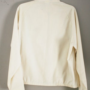 Puede incluir: Una chaqueta blanca con cremallera, mangas largas y un cord&oacute;n en la parte inferior.