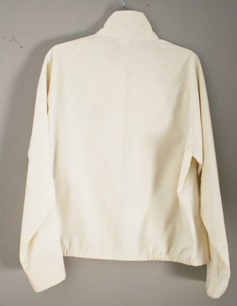 Puede incluir: Una chaqueta blanca con cremallera, mangas largas y un cord&oacute;n en la parte inferior.