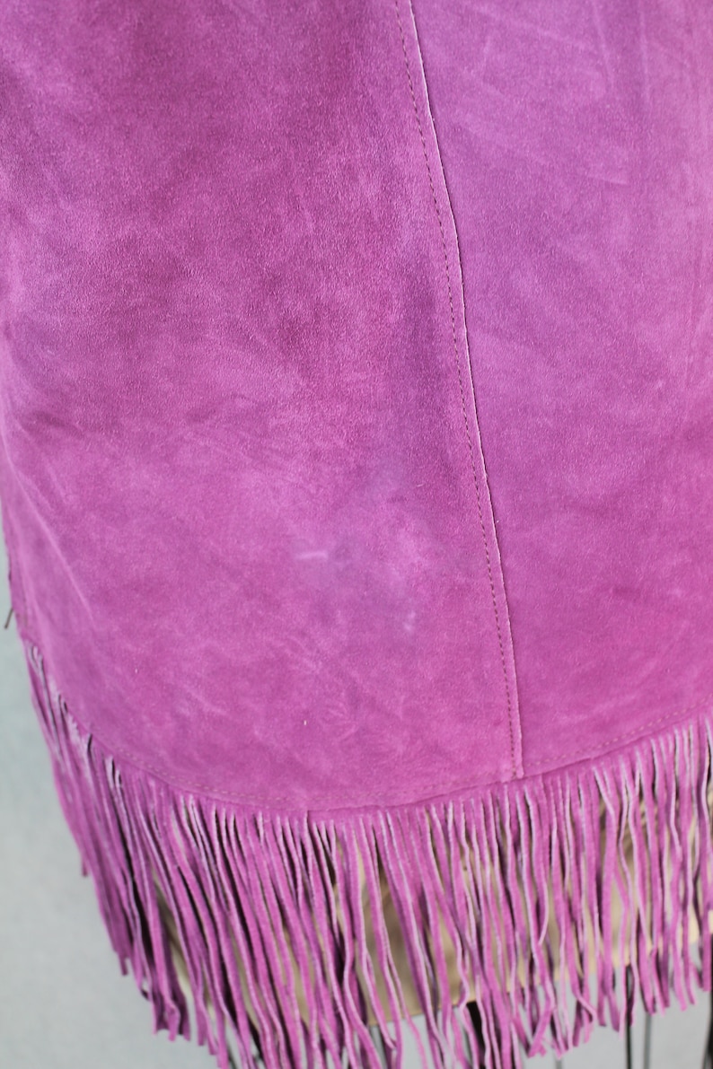May include: A purple suede skirt with a fringe hem. The skirt has a seam down the back.