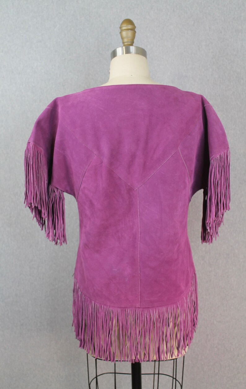 May include: A purple suede top with fringe detailing on the sleeves and hem.