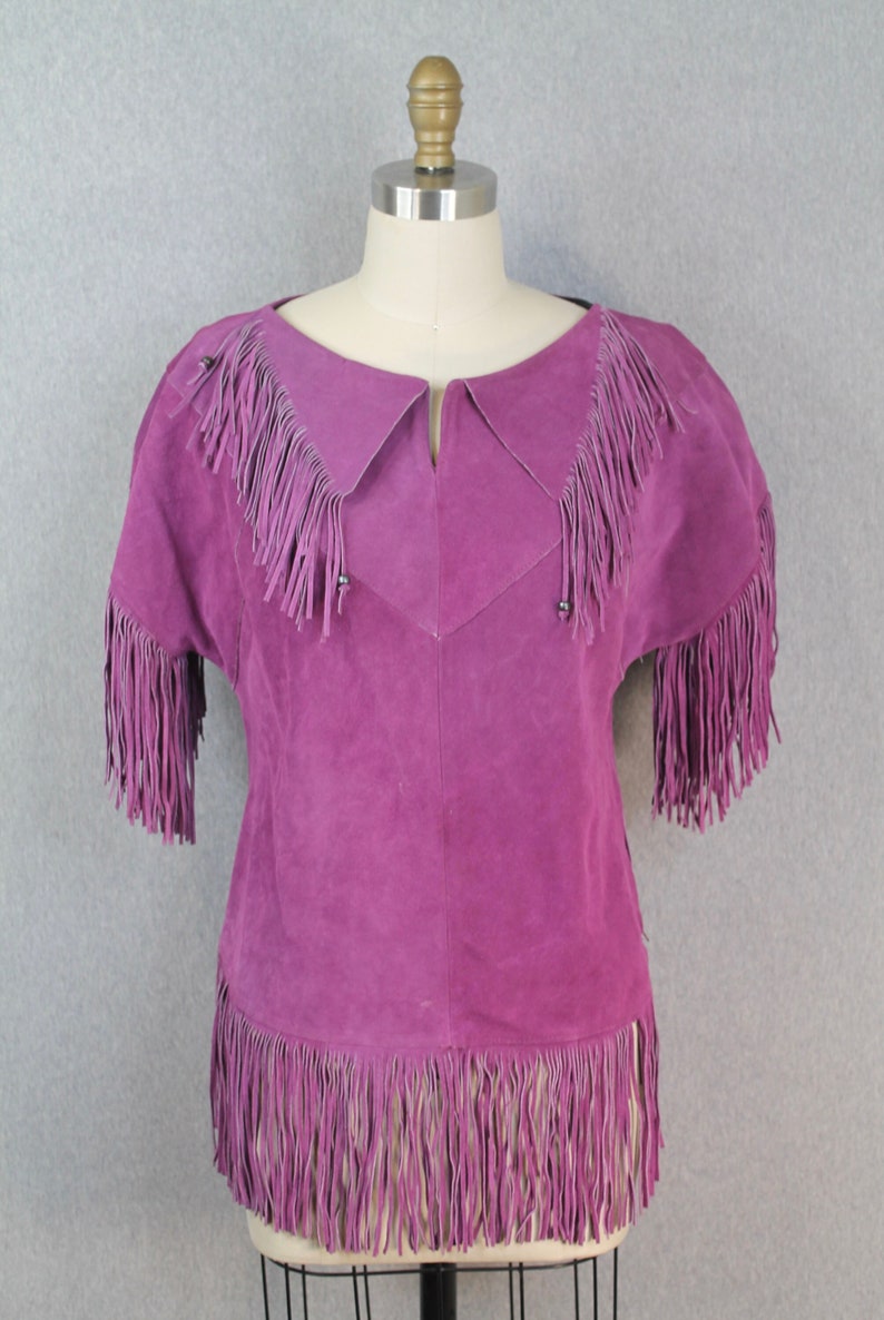 May include: A purple suede top with fringe detailing around the neckline, sleeves, and hem.