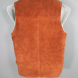 May include: A brown suede vest with a white faux fur lining. The vest has a zipper closure and a stand-up collar.