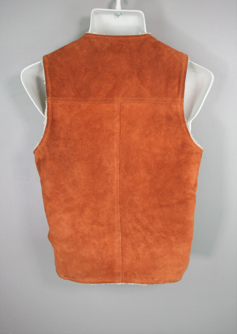 May include: A brown suede vest with a white faux fur lining. The vest has a zipper closure and a stand-up collar.