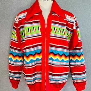 May include: A red zip-up jacket featuring a vibrant horizontal pattern of lime green, bright blue, yellow, and white stripes with geometric shapes. The jacket has a wide collar, long sleeves with elastic cuffs, and a full-length front zipper closure.
