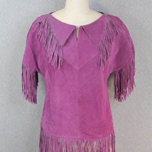 May include: A purple suede top with fringe detailing around the neckline, sleeves, and hem.