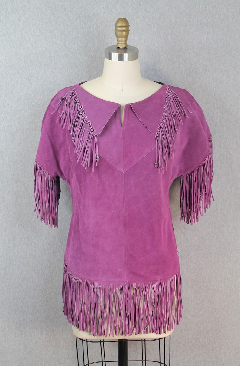 May include: A purple suede top with fringe detailing around the neckline, sleeves, and hem.