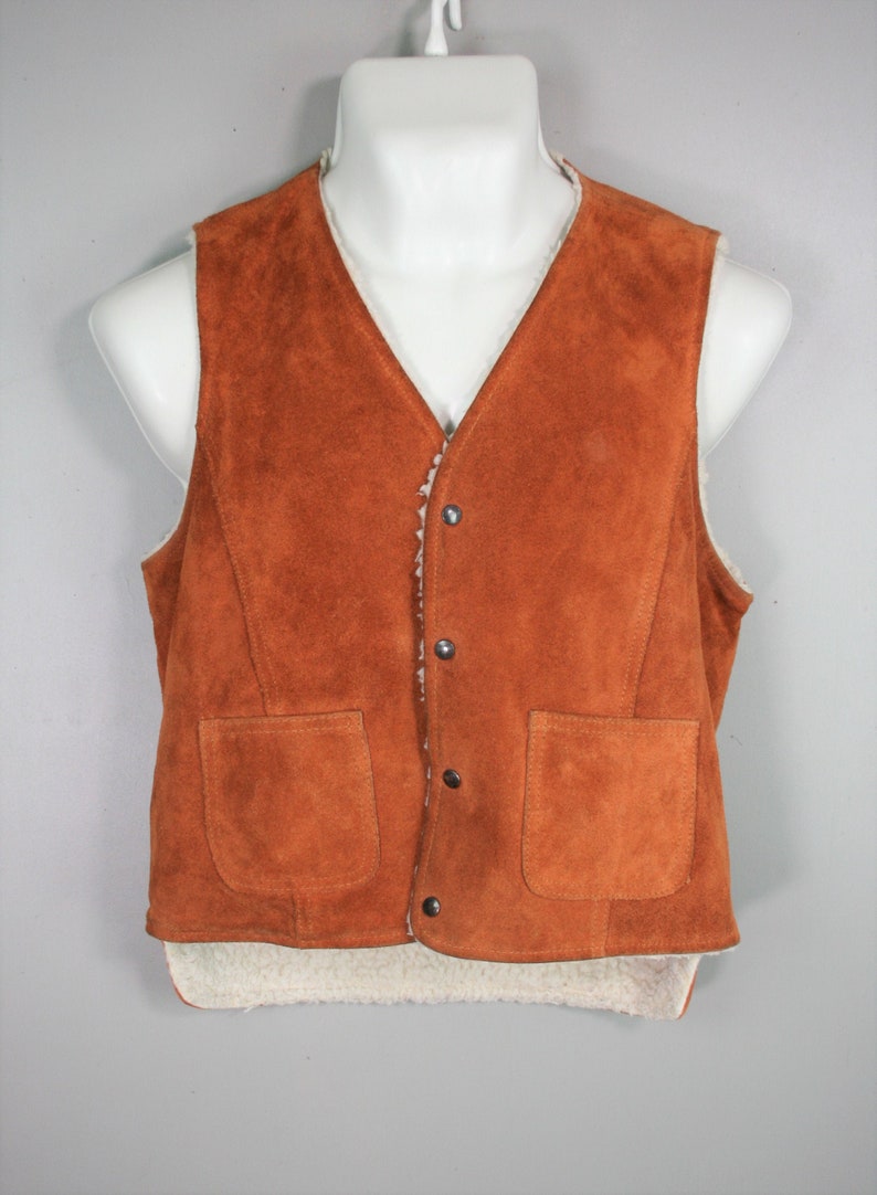 May include: A brown suede vest with a sherpa lining and two front pockets. The vest has a button closure.