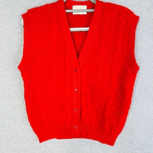 May include: A bright red sleeveless knit sweater vest featuring a V-neckline, a vertical cable knit pattern, and a front button closure with four matching red buttons. The garment has ribbed trim along the armholes, neckline, and hem.