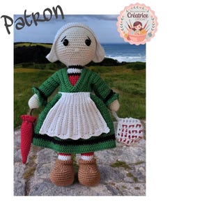 Peut inclure: Poupée au crochet portant une robe verte, un tablier blanc et une coiffe blanche. La poupée tient un parapluie rouge et un panier. La poupée est debout sur une surface herbeuse verte. L'image comprend également le texte "Patron" en haut à gauche et un logo avec le texte "Créatrice Crochet" en haut à droite.
